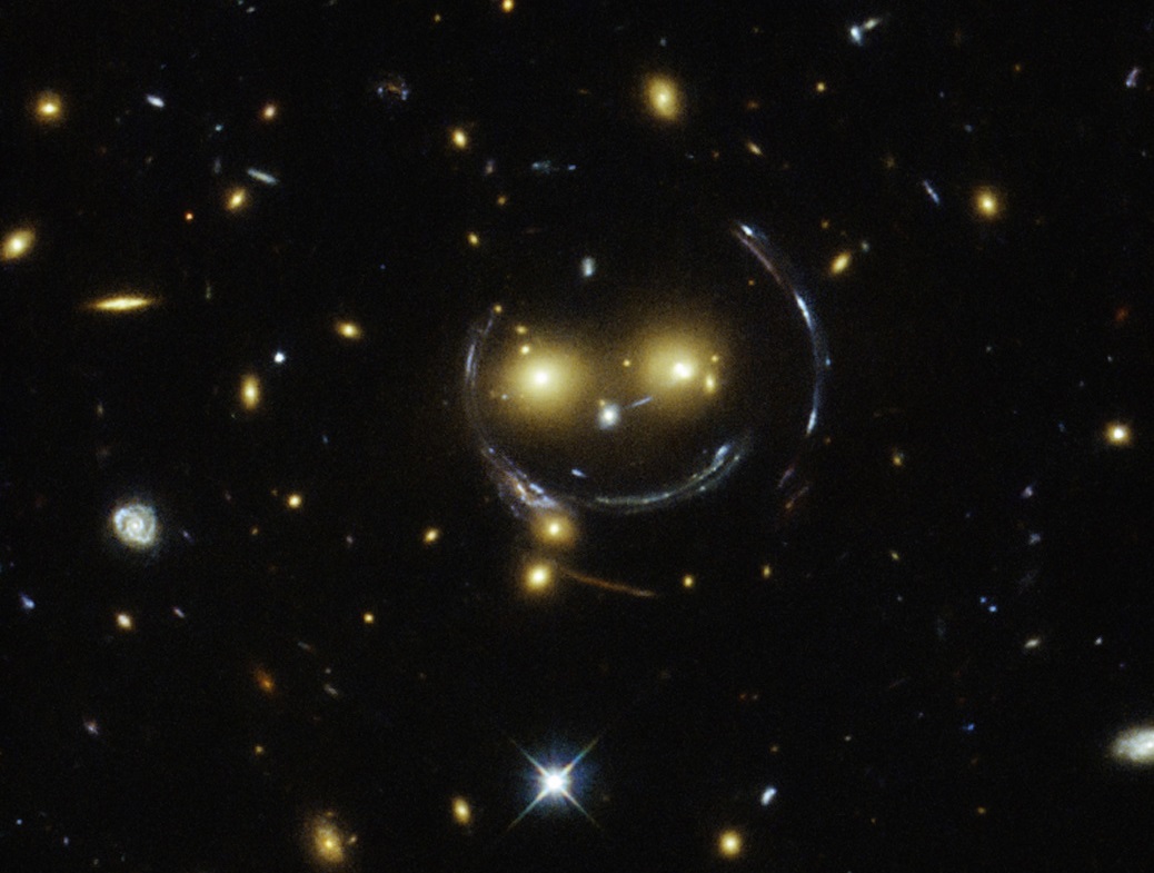 עיני ה"סמיילי" הן 2 גלקסיות. קשת החיוך- האור שמגיע מאחוריהן, מתעוות ומועצם כבזכוכית מגדלת, בזכות הכבידה של אותן גלקסיות|NASA/ESA